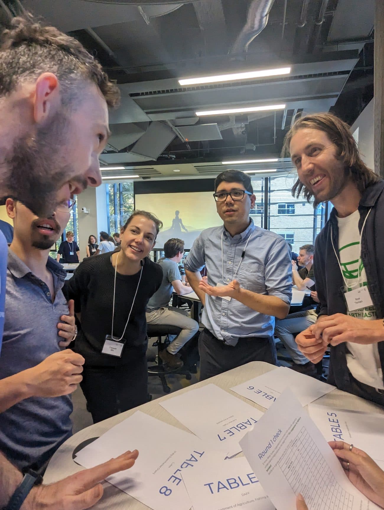 Players laugh over a Round 1 check sheet, holding the estimative-probability table used to set their dice roll.